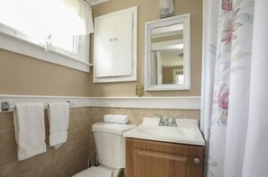 A bathroom with a toilet, sink, and mirror. There are towels hanging on a rack and a shower curtain with a floral pattern. - Cozy Cottage in Eastham near National Seashore (Eastham)