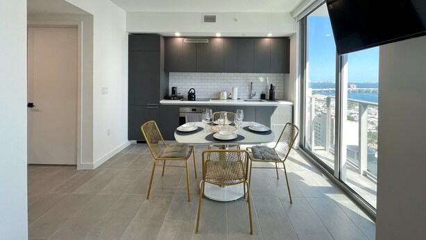 A modern kitchen with dark cabinets, white countertops, and a dining area with a round table and four chairs. - AM2212 DOWNTOWN MIAMI, GREAT VIEWS STUDIO (Miami)