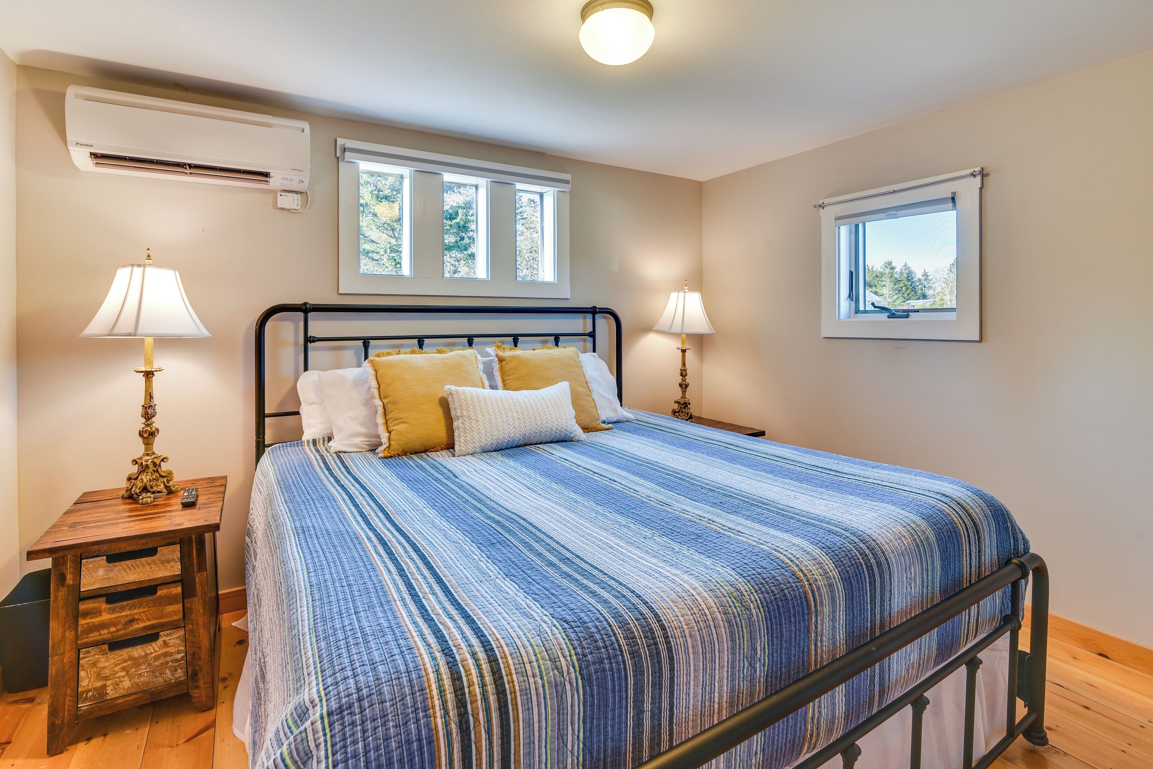 A bedroom with a bed, two bedside tables with lamps, a window, and an air conditioning unit.
