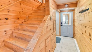 Una escalera de madera que lleva a una puerta con un ventanal pequeño, una lámpara en el techo y un estante de metal en la pared.