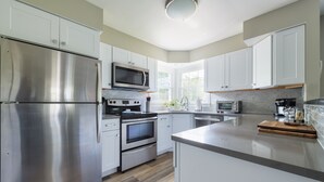 Una cocina moderna con electrodomésticos de acero inoxidable, armarios blancos y piso de madera.