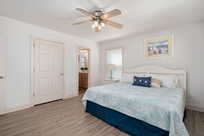A bedroom with a bed, a ceiling fan, a window with blinds, and a door.