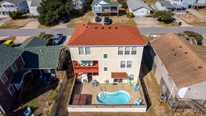 A two-story house with a red roof, a backyard with a swimming pool, and a covered patio area.
