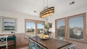 A dining area with a wooden table, chairs, a hanging light fixture, and a view through the windows.