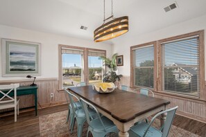 A dining area with a wooden table, chairs, a hanging light fixture, and a view through the windows.