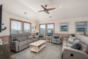 A spacious living room with a ceiling fan, large windows, and a view of the ocean.