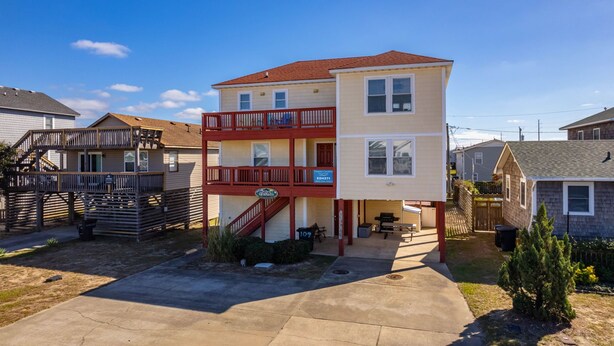 A multi-story residential building with a balcony, a covered patio, and a front yard.