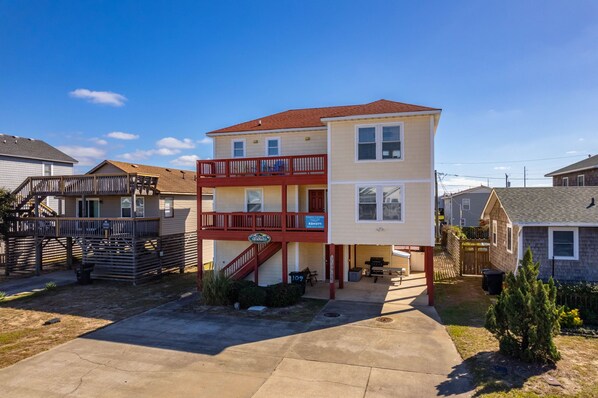 A multi-story residential building with a balcony, a covered patio, and a front yard.