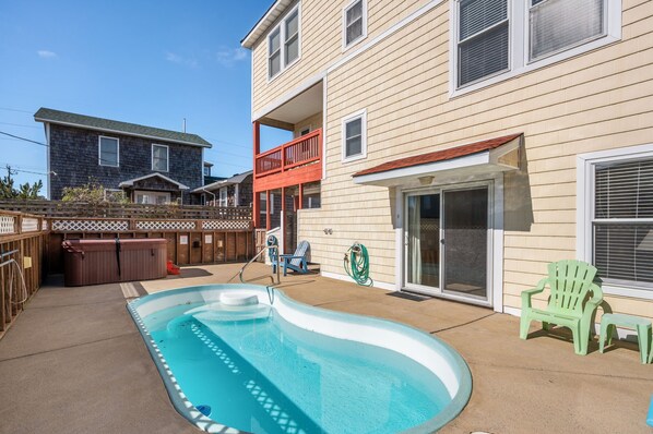 A backyard with a swimming pool, a hot tub, and a covered patio area.
