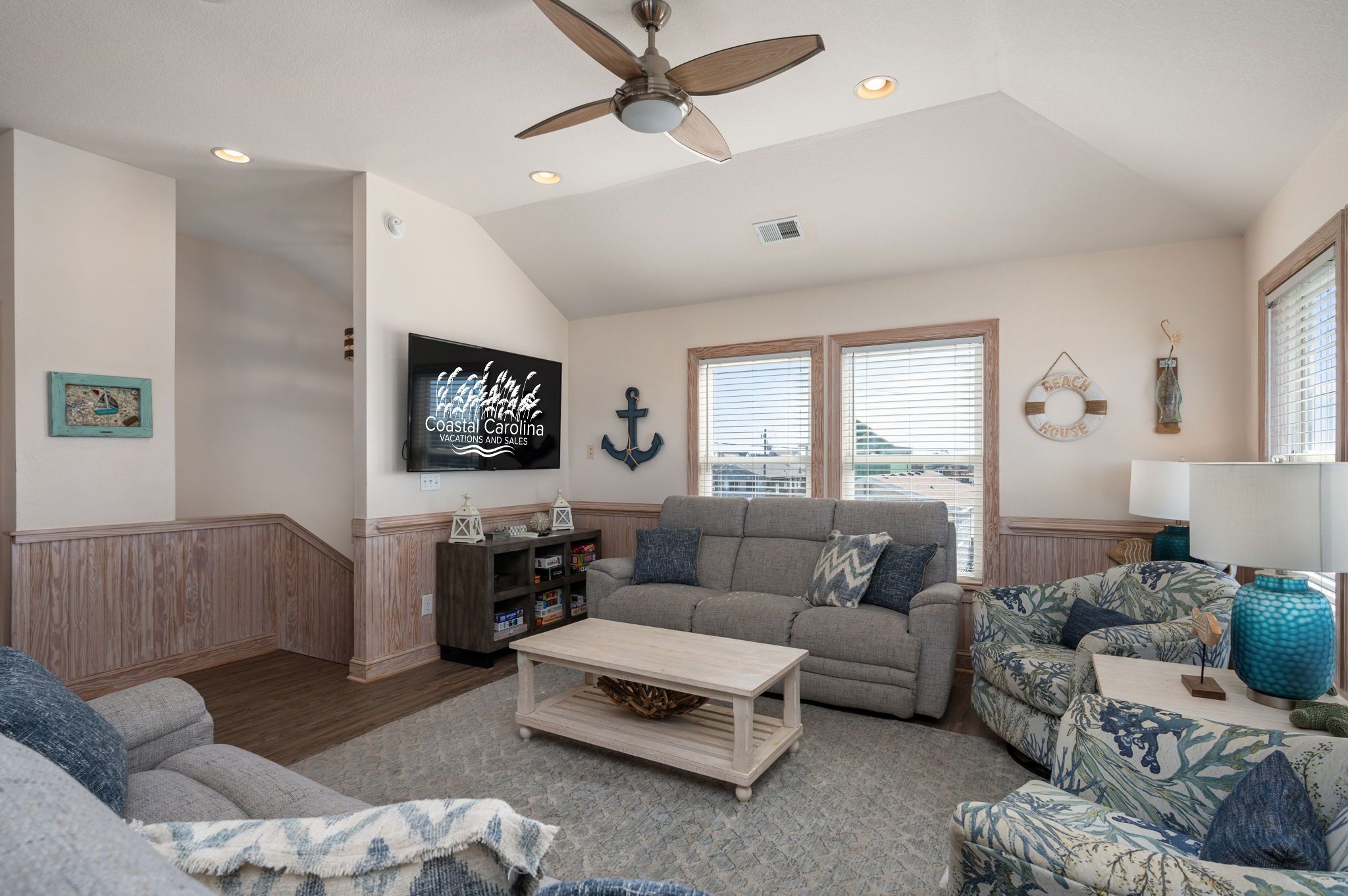 A living room with a ceiling fan, a television, a couch, a coffee table, and a window with blinds.