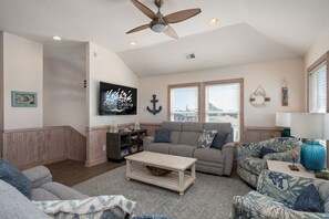 A living room with a ceiling fan, a television, a couch, a coffee table, and a window with blinds. - The Gorbals:Oceanside, pool, hot tub, close to the beach & Wright Bro's Memorial (Kill Devil Hills)