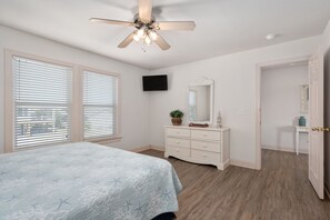 A bedroom with a bed, dresser, mirror, television, and a ceiling fan. - The Gorbals:Oceanside, pool, hot tub, close to the beach & Wright Bro's Memorial (Kill Devil Hills)