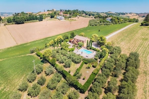 An aerial view of a countryside property with a large house, a swimming pool, and surrounding fields.
