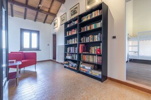 Ein geräumiger Raum mit einer großen Bücherwand, einem roten Sofa und einem Fenster, das für natürliches Licht sorgt.