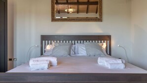 Una cama bien hecha con almohadas a rayas y dos toallas dobladas, un cabecero de madera y un espejo arriba.