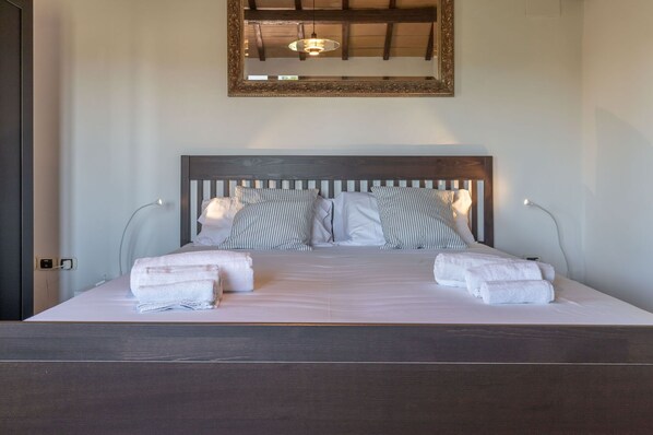 Una cama bien hecha con almohadas a rayas y dos toallas dobladas, un cabecero de madera y un espejo arriba.