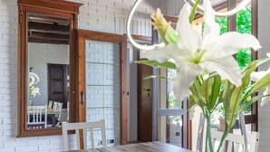 Un comedor con una mesa de madera, sillas blancas, un espejo y una pared de ladrillo blanco.