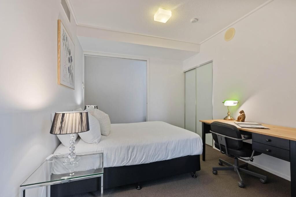 A bedroom with a bed, a desk, a chair, a lamp, and a mirror.