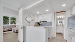 A modern kitchen with white cabinetry, a central island, and a dining area with a sofa and table.