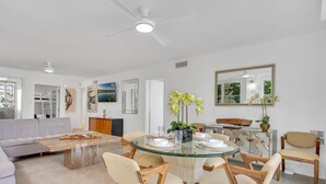 A modern living room with a glass dining table, beige sofas, and wooden chairs.