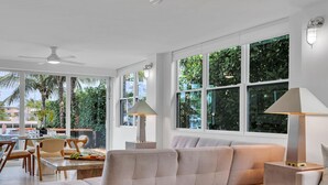 A spacious living area with a large window, a ceiling fan, and a dining area with chairs and a table.