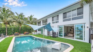 A modern house with a swimming pool, outdoor furniture, and palm trees.