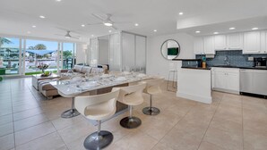 Una cocina moderna con armarios blancos, una isla central con taburetes de bar y una zona de comedor con una mesa grande dispuesta para seis personas.
