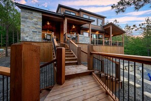 A modern wooden house with a stone exterior, a wooden deck, and a staircase leading to a covered porch. - EV Outlet , Hot Tub, Firepit, Playset, Pool Table, Creek (Broken Bow)