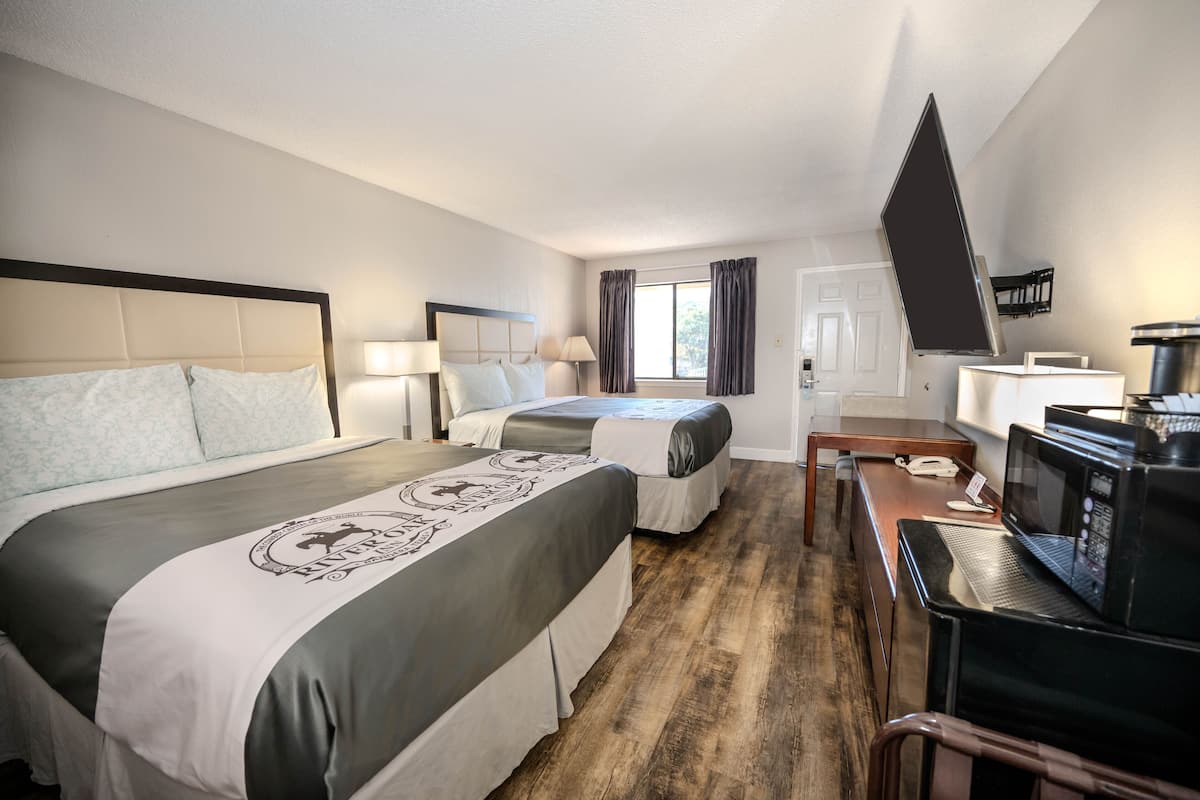 A hotel room with two beds, a desk with a laptop, a microwave, and a TV.