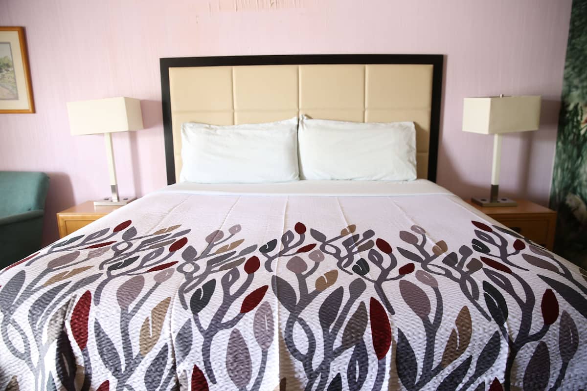 A hotel room with a bed, two bedside lamps, a nightstand, and a green chair.