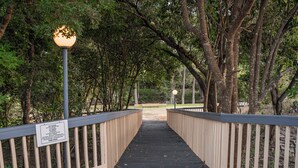 A wooden bridge with a sign on the left, surrounded by trees. - River Oak Inn (Bandera)