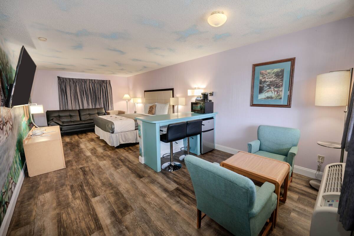 A compact hotel room with a bed, a desk, a chair, a small table, a TV, and a heater.