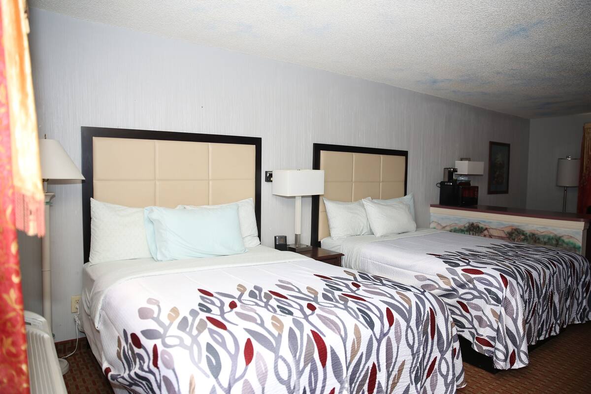 A hotel room with two beds, each with a headboard, bedside tables, lamps, and a mirror.