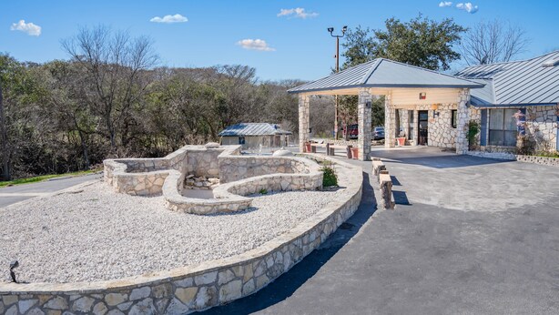 A stone structure with a gazebo, a paved area, and a building with a metal roof. - River Oak Inn (Bandera)