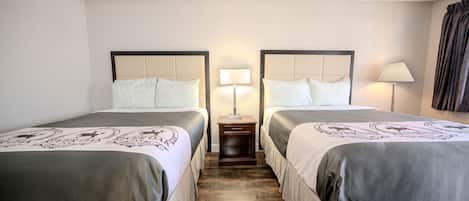 A hotel room with two beds, each with a headboard, bedside tables with lamps, and a wooden floor.