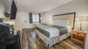 A hotel room with a bed, bedside tables, a TV, and a microwave. - River Oak Inn (Bandera)