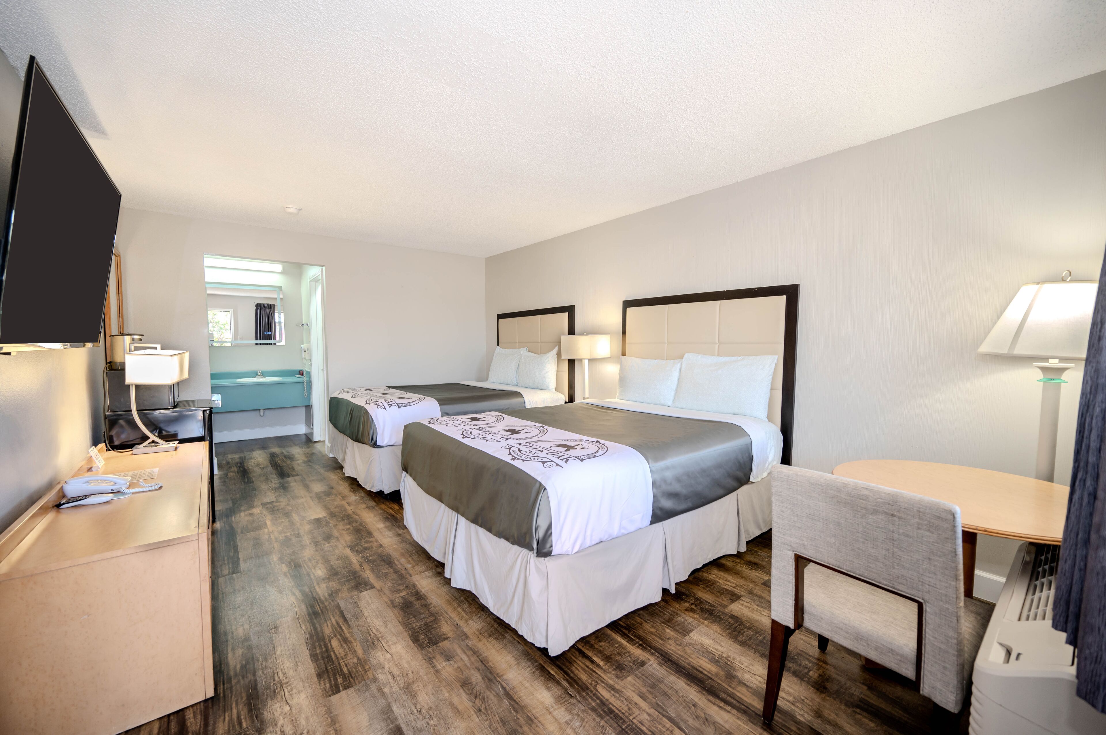 A hotel room with two beds, a desk, a chair, and a television.