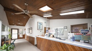 A reception area with wooden paneling, a reception desk, framed pictures, and a sign thanking customers for shopping small. - River Oak Inn (Bandera)