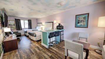 Habitación de hotel con una cama, un escritorio con dos sillas, una mesita, un televisor y un cuadro en la pared.