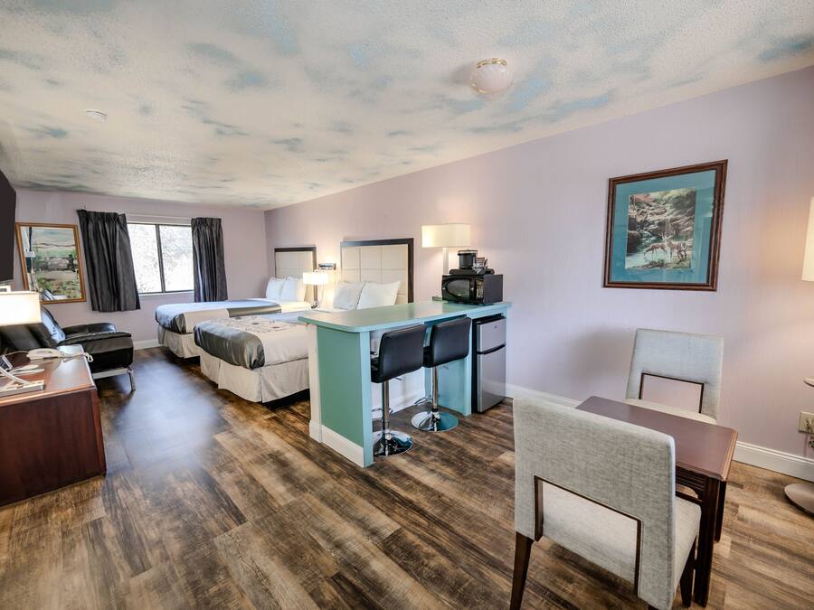 Habitación de hotel con una cama, un escritorio con dos sillas, una mesita, un televisor y un cuadro en la pared.