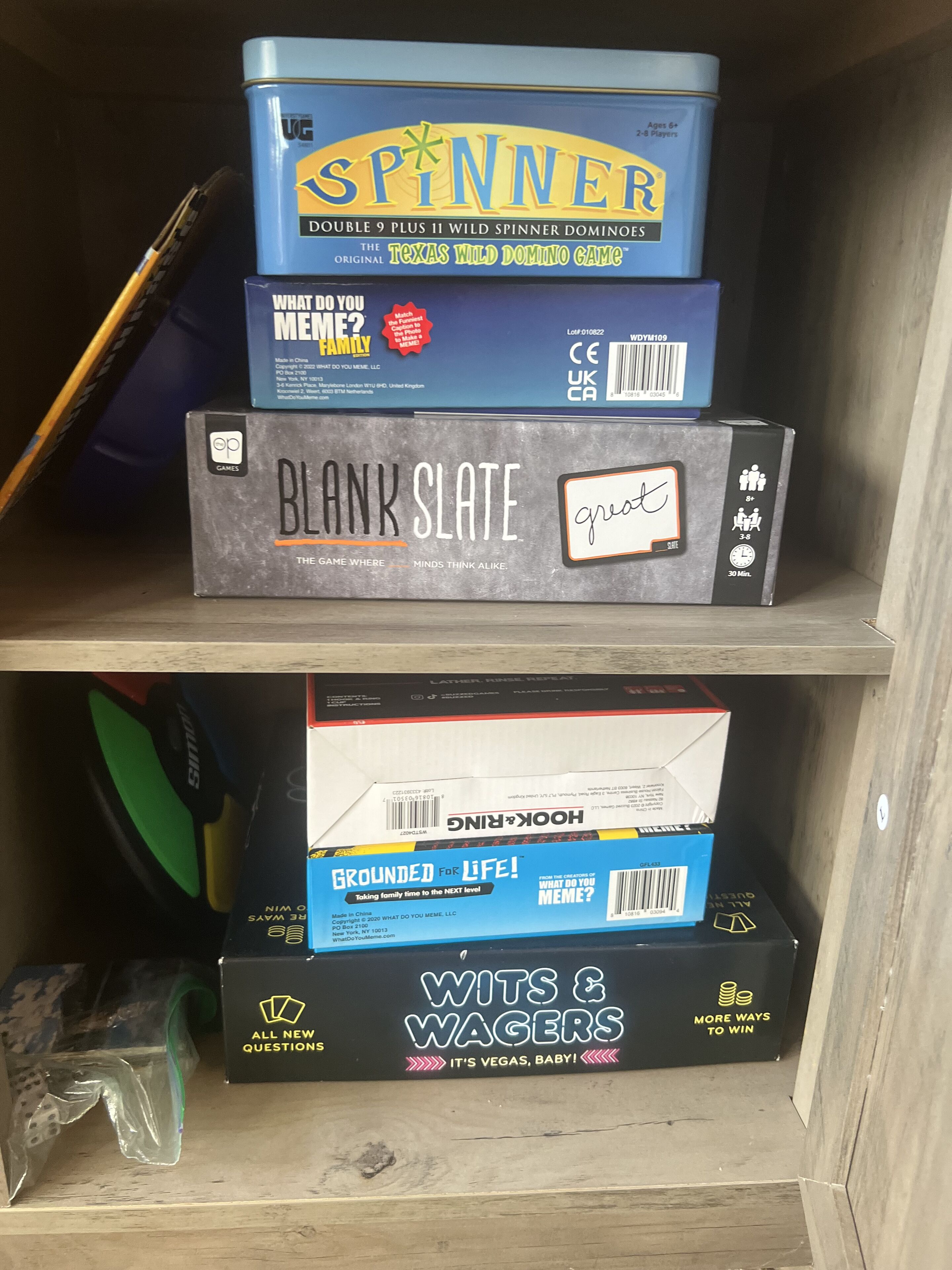 Een plank met verschillende gezelschapsspellen, waaronder 'SPINNER', 'BLANK SLATE', 'HOOK&LINE' en 'WITS & WAGERS'.