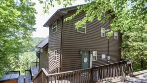 A two-story wooden cabin with a balcony, surrounded by trees.