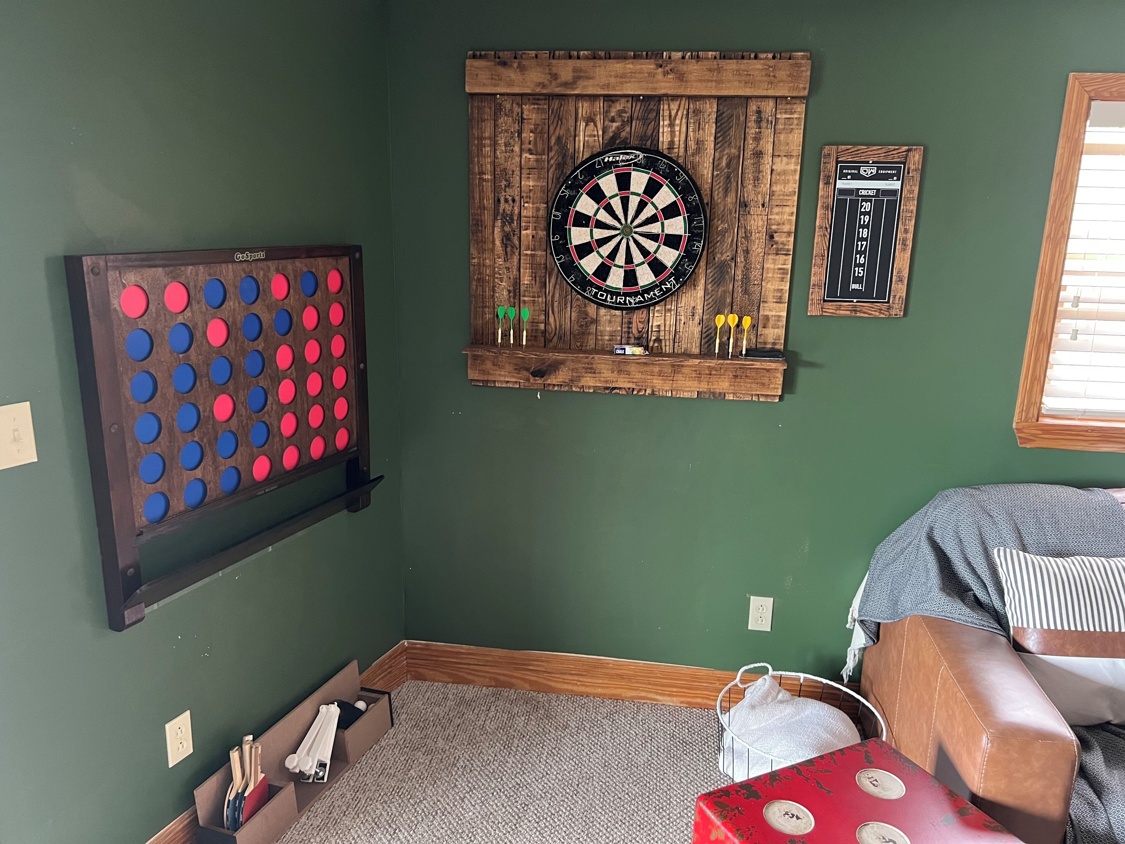 A room with a dartboard, a board game, and a cricket score display.