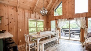 A wooden cabin interior with a dining table, chairs, a bench, and a chandelier.