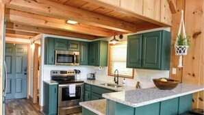 A spacious kitchen with wooden beams, green cabinets, and a central island with stools.