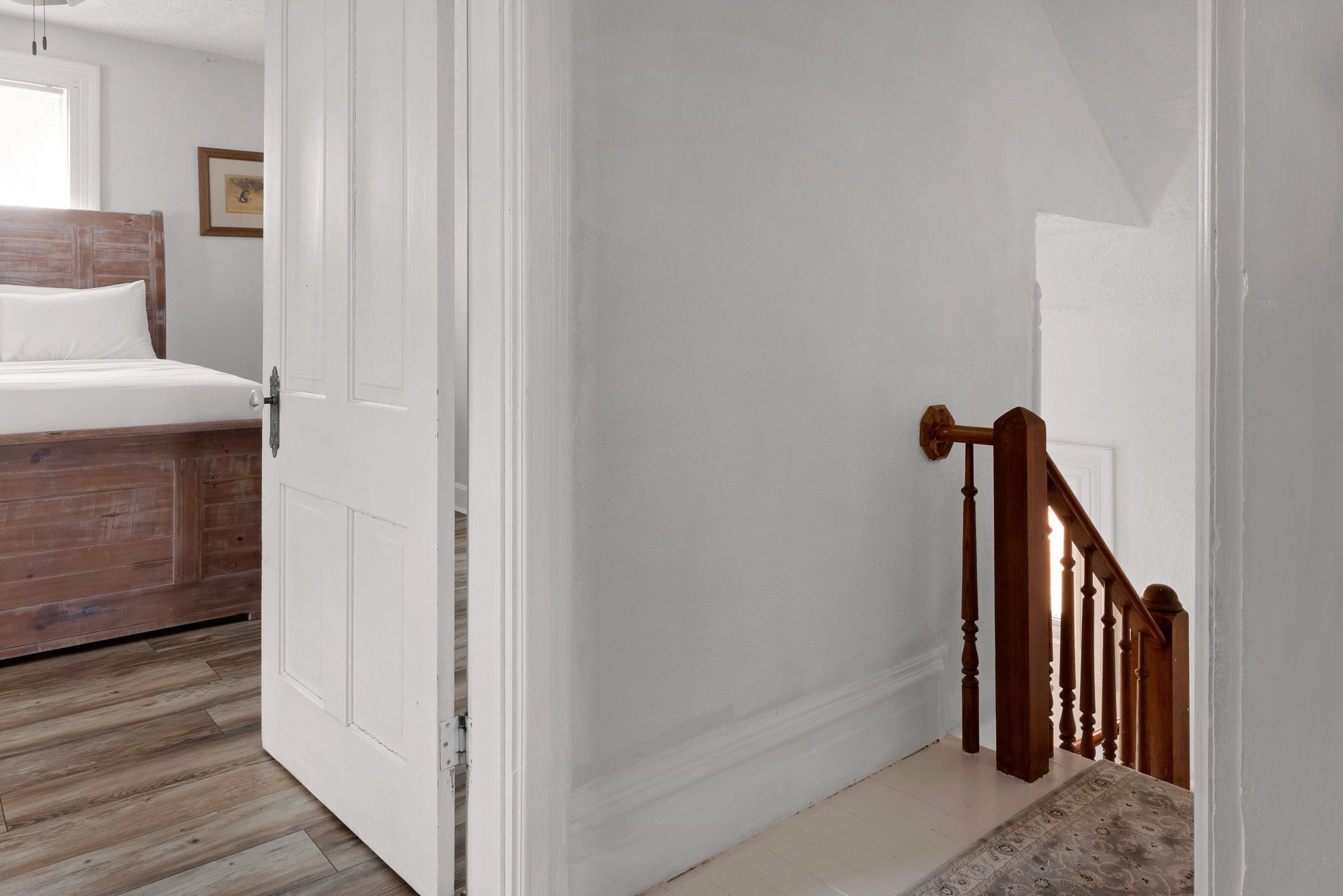 Un dormitorio con cabecera de madera, una puerta blanca y una escalera con barandillas de madera.