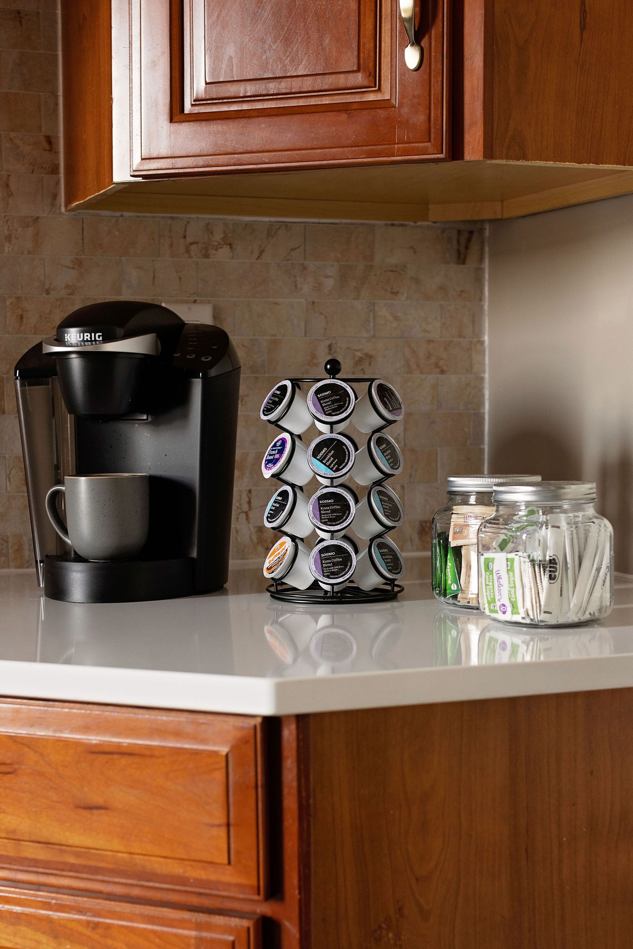 Une machine à café, un support pour dosettes de café et des pots remplis de dosettes de café, le tout posé sur un plan de travail de cuisine.