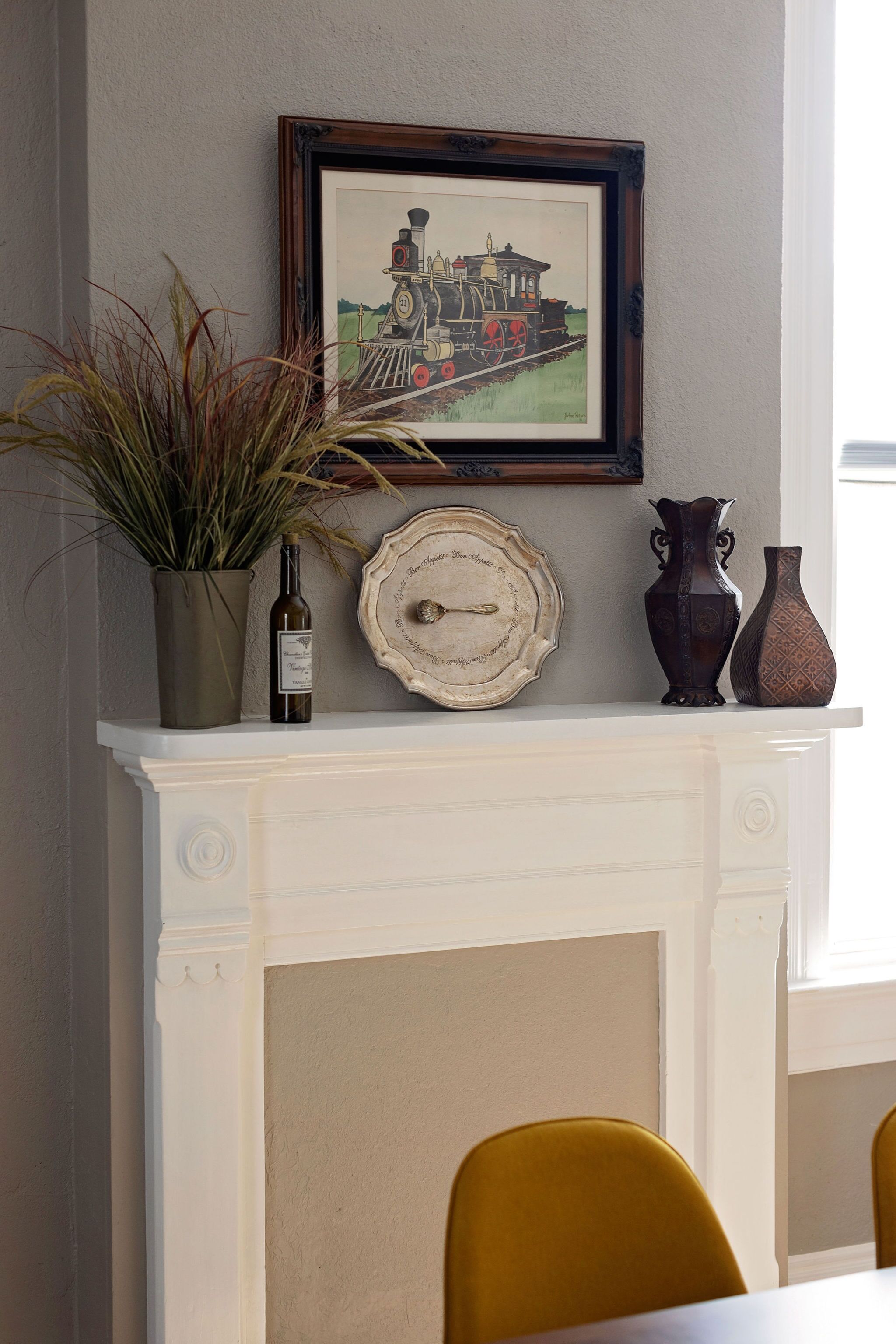 A fireplace mantel with a framed train painting, a wine bottle, and decorative vases.