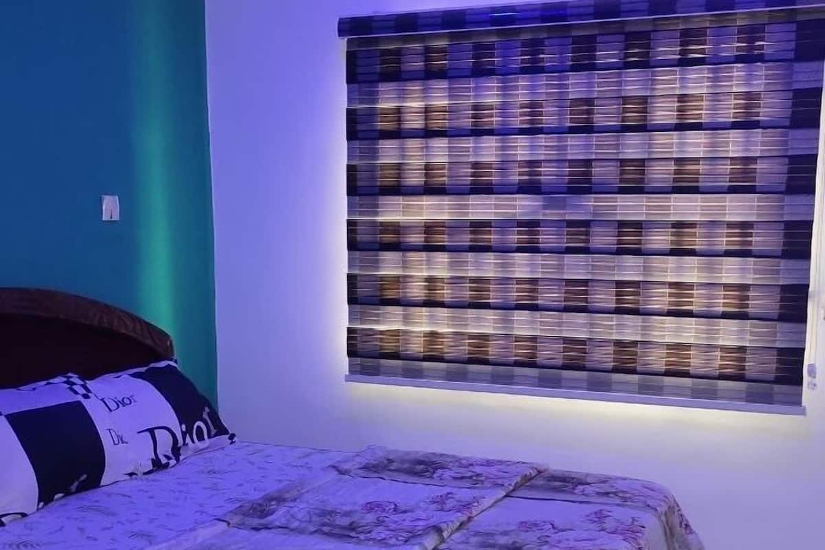 A bedroom with a bed, a wall-mounted light, and a window with a patterned blind.