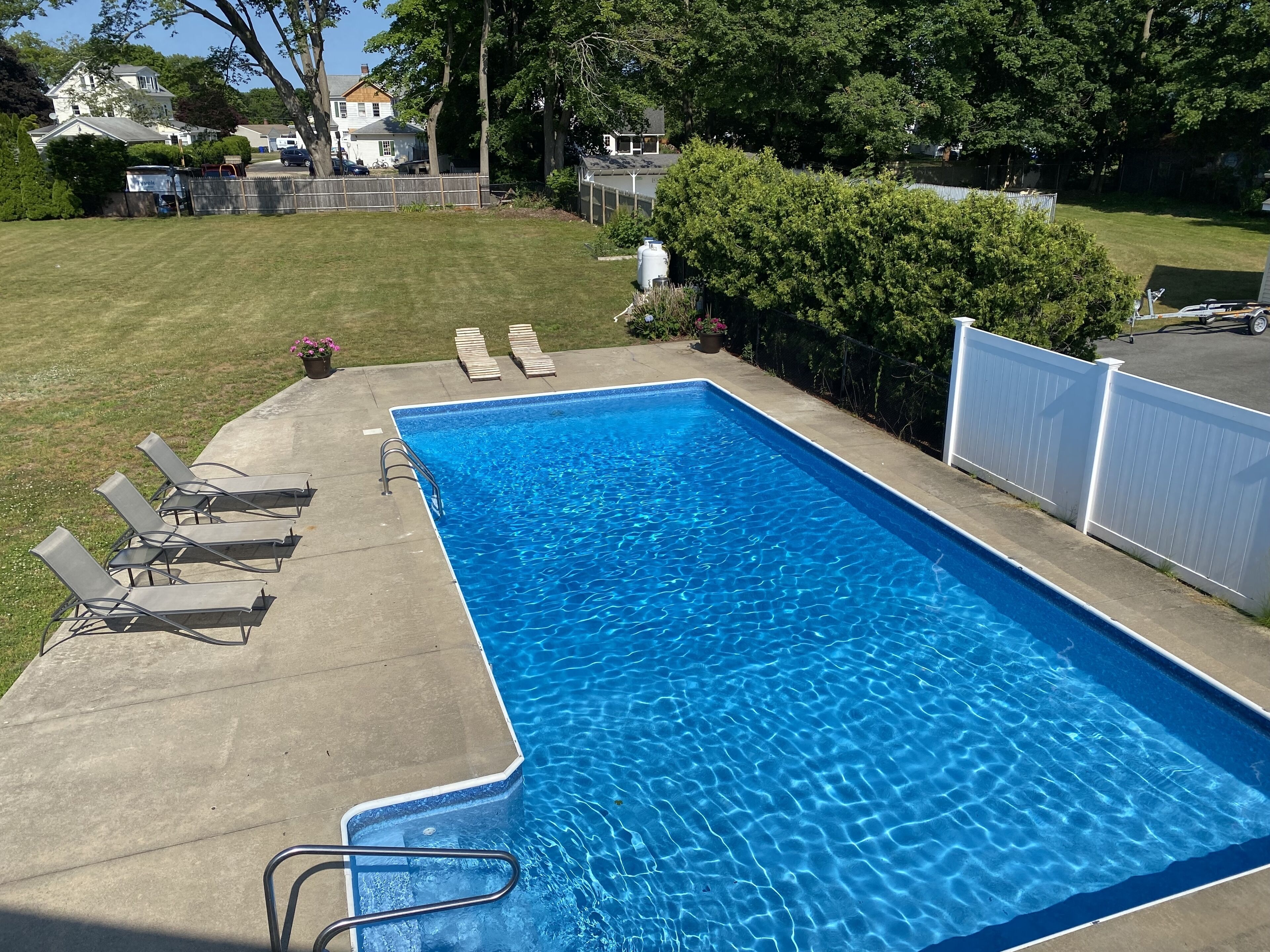 Ein rechteckiger Pool mit klarem, blauem Wasser, umgeben von einer Betonplattform und einem weißen Zaun.